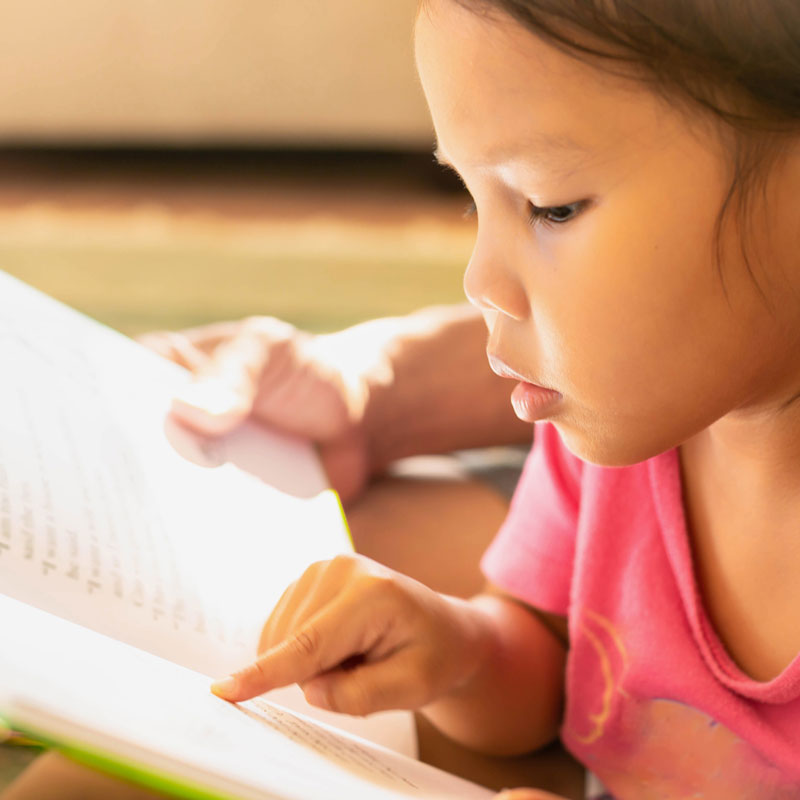 little girl following along with book