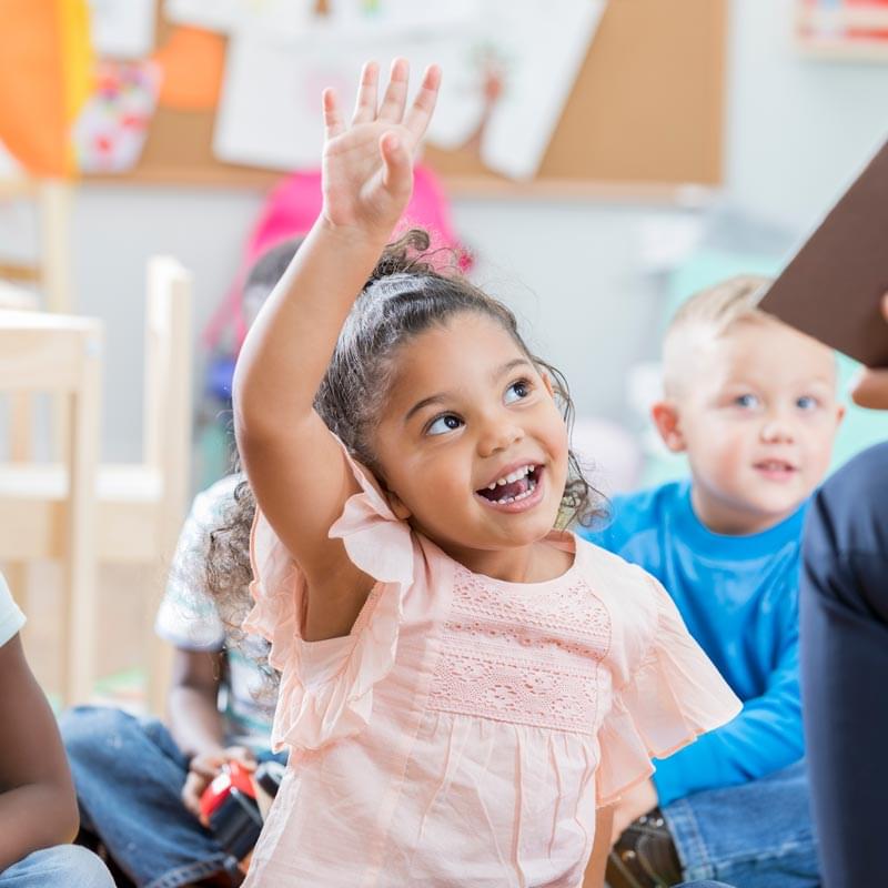 little girl raising her hand in classroom